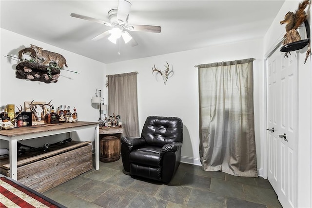 living area with stone finish flooring, baseboards, and ceiling fan