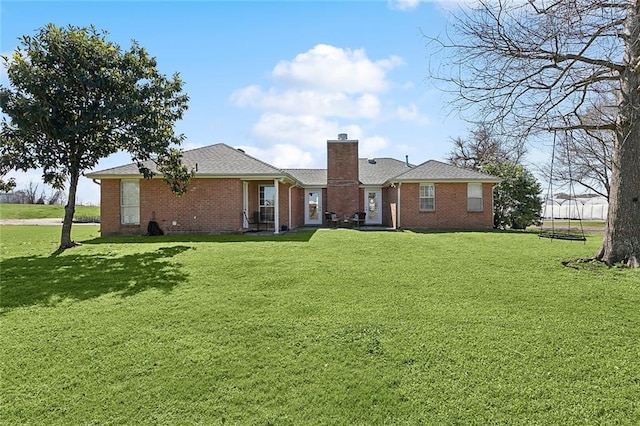 rear view of property featuring brick siding, a lawn, and a chimney