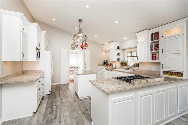 kitchen featuring a center island, decorative light fixtures, white cabinetry, sink, and light stone counters