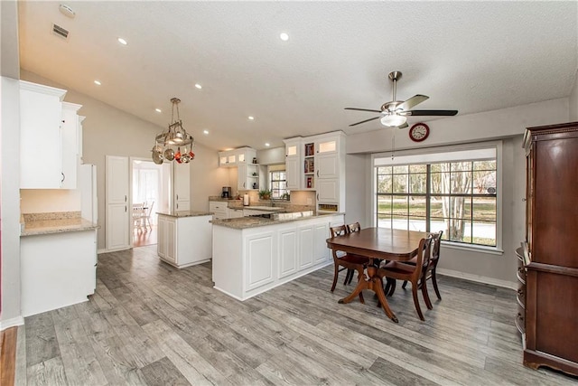 kitchen featuring white cabinets, lofted ceiling, a kitchen island, hanging light fixtures, and light wood-type flooring