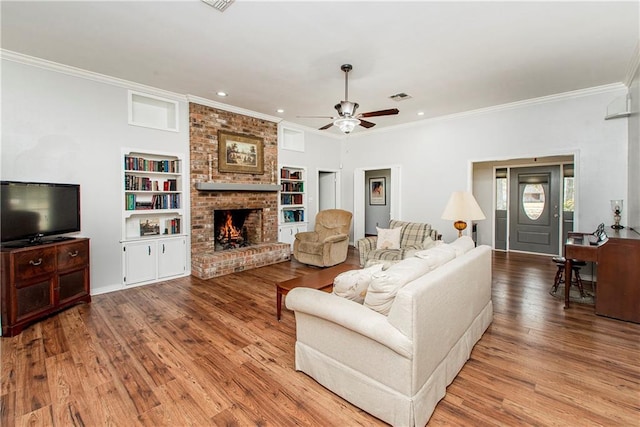 living room featuring a brick fireplace, light hardwood / wood-style floors, built in shelves, and ornamental molding