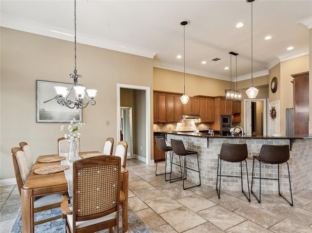 kitchen featuring hanging light fixtures, ornamental molding, tasteful backsplash, and a breakfast bar