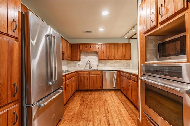 kitchen featuring light wood-type flooring, visible vents, a sink, stainless steel appliances, and brown cabinetry