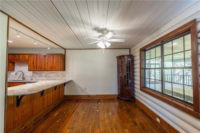 kitchen featuring brown cabinetry, baseboards, a sink, dark wood-type flooring, and backsplash