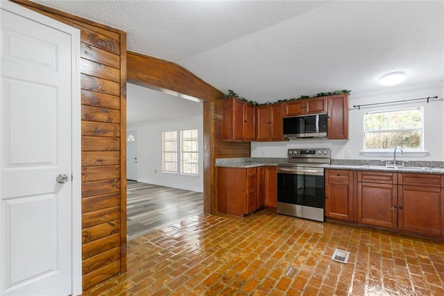 kitchen with lofted ceiling, stainless steel appliances, sink, and a textured ceiling