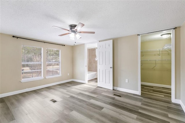 unfurnished bedroom with hardwood / wood-style flooring, a spacious closet, ceiling fan, ensuite bath, and a closet