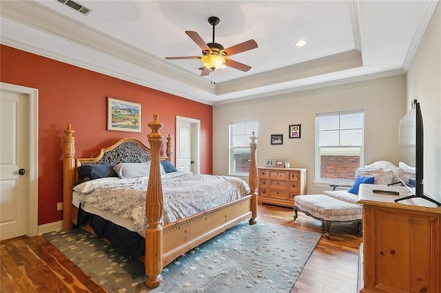 bedroom featuring hardwood / wood-style flooring, ornamental molding, ceiling fan, and a tray ceiling