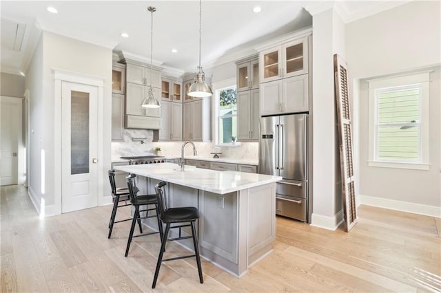 kitchen with a breakfast bar, a center island with sink, light wood-type flooring, high quality fridge, and decorative backsplash