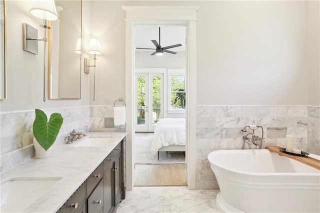 bathroom featuring ceiling fan, a tub to relax in, vanity, and tile walls