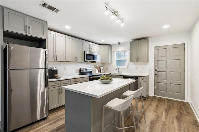 kitchen featuring a kitchen bar, appliances with stainless steel finishes, gray cabinetry, a kitchen island, and dark wood-type flooring