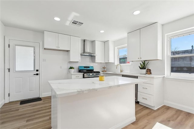 kitchen featuring light hardwood / wood-style flooring, white cabinetry, wall chimney range hood, a kitchen island, and gas stove