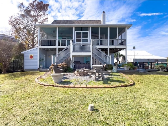 rear view of house with a sunroom, a fire pit, and a yard