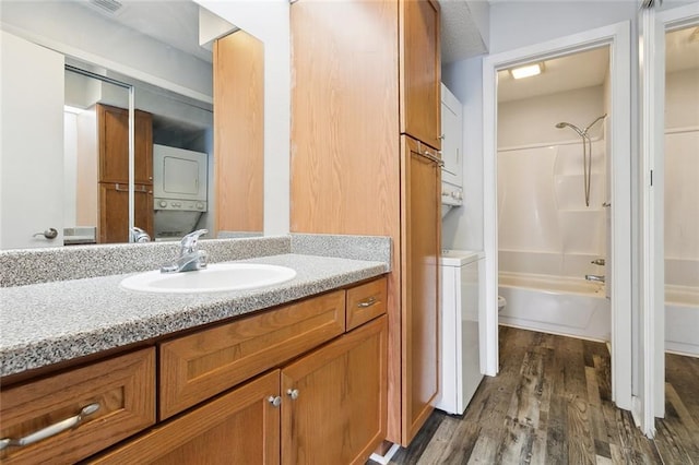 full bathroom featuring hardwood / wood-style flooring, bathtub / shower combination, toilet, stacked washer / drying machine, and vanity