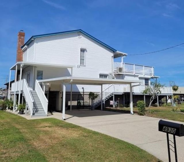 rear view of property featuring a yard, driveway, and stairs