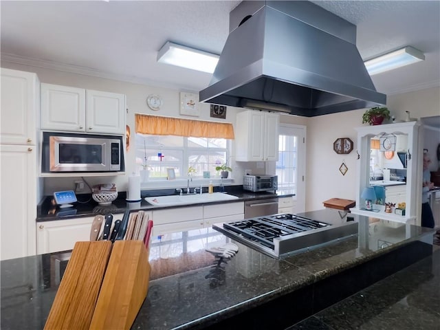 kitchen featuring island range hood, dark stone counters, stainless steel appliances, white cabinetry, and a sink