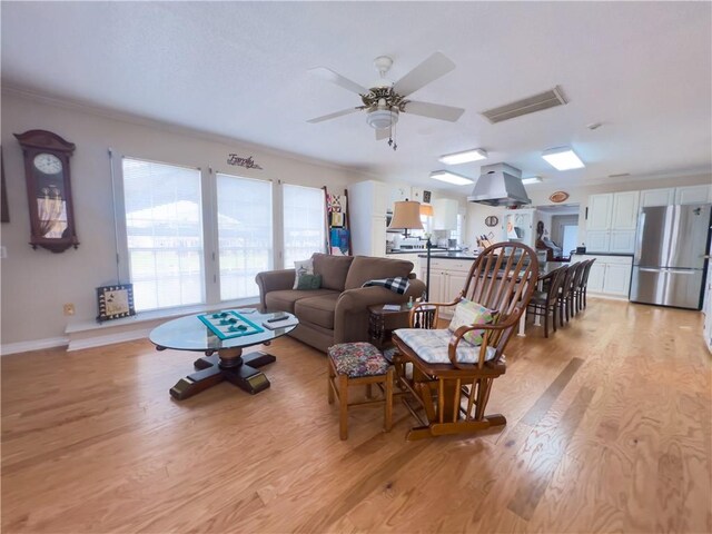 living room with crown molding, a textured ceiling, a brick fireplace, light wood-type flooring, and ceiling fan