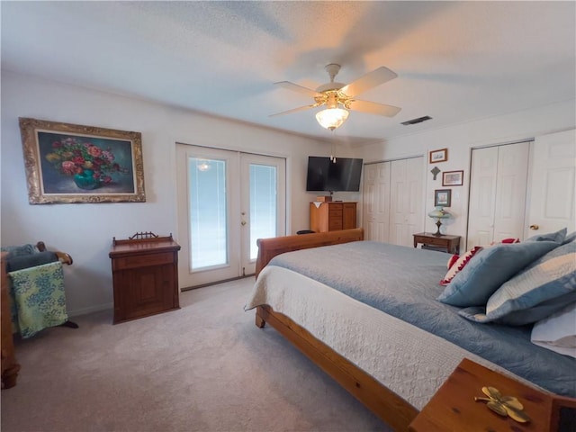 carpeted bedroom featuring access to exterior, french doors, two closets, visible vents, and a ceiling fan