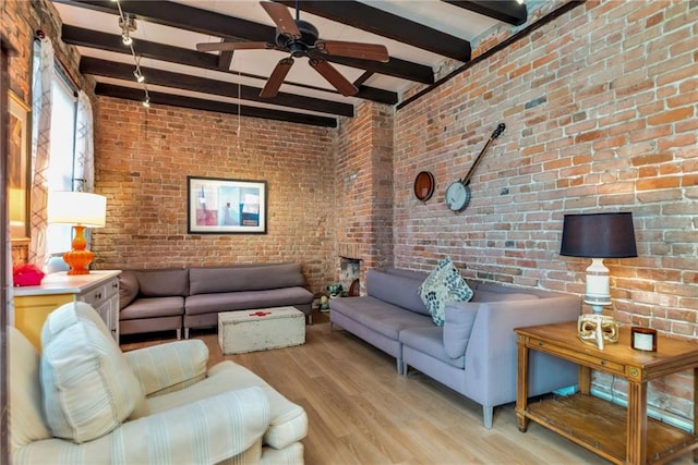 living room featuring beamed ceiling, brick wall, ceiling fan, and light hardwood / wood-style flooring