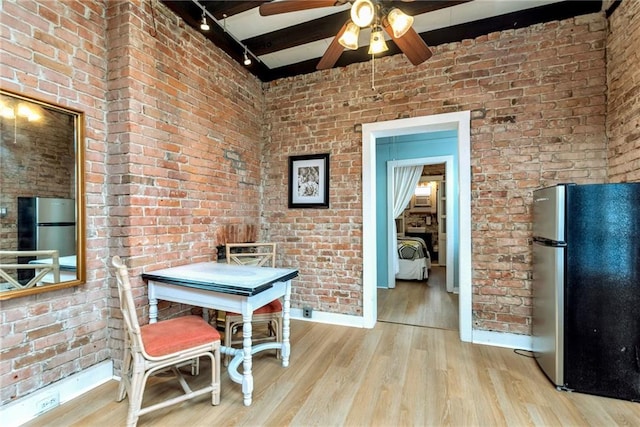 unfurnished dining area featuring beamed ceiling, brick wall, and light hardwood / wood-style flooring