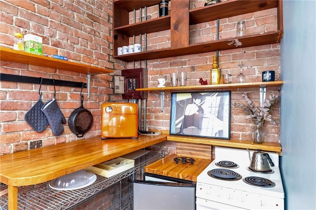 kitchen with white electric stove, cooktop, and brick wall