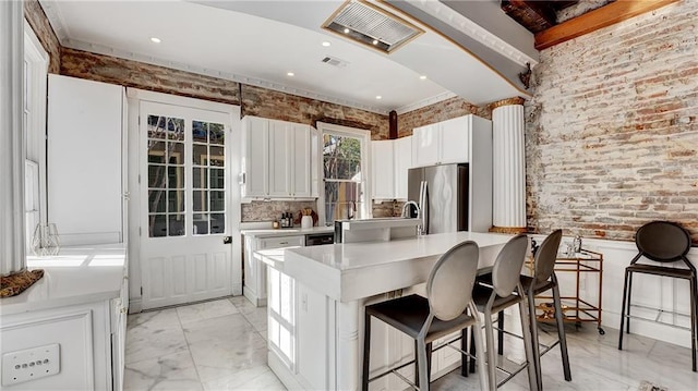 kitchen featuring stainless steel fridge, a breakfast bar, white cabinets, and brick wall