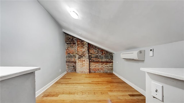 interior space with brick wall, lofted ceiling, a wall mounted air conditioner, and light hardwood / wood-style flooring