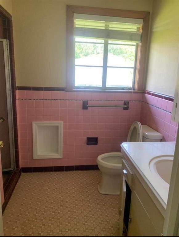 bathroom featuring vanity, toilet, tile walls, and walk in shower