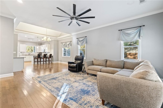 living room featuring ornamental molding, ceiling fan with notable chandelier, light hardwood / wood-style floors, and a tray ceiling