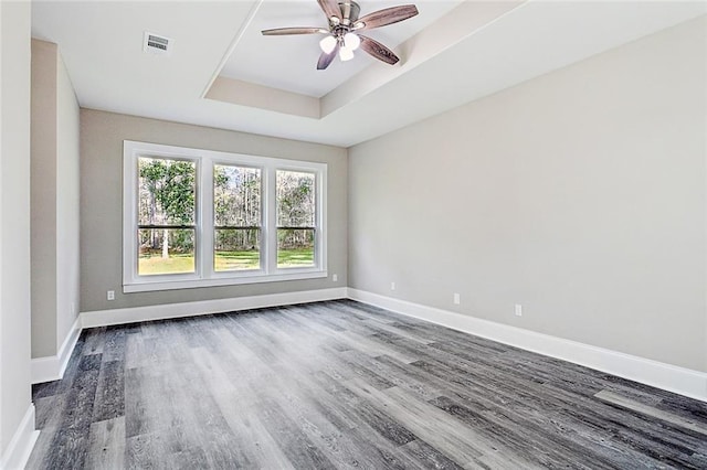 empty room featuring a raised ceiling, hardwood / wood-style floors, and ceiling fan