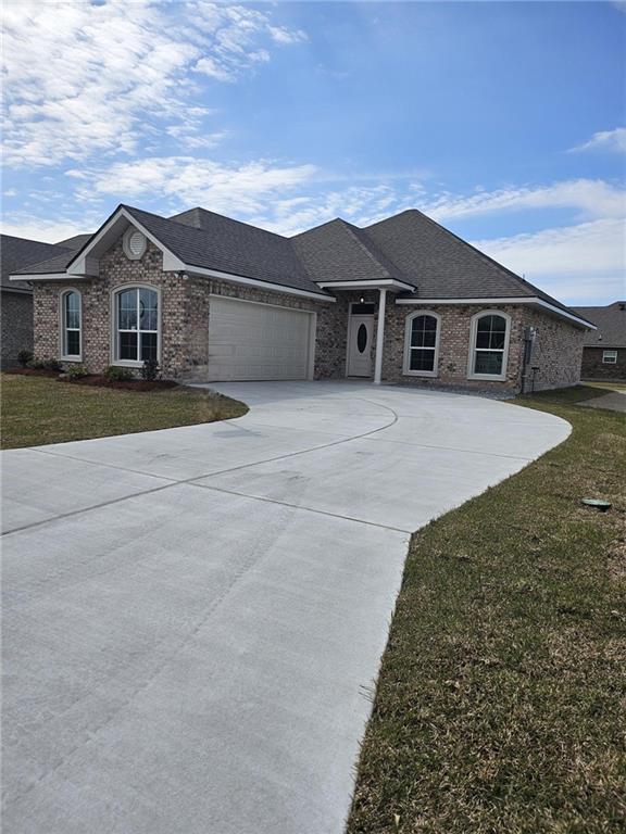 view of front facade with an attached garage, brick siding, a shingled roof, driveway, and a front yard