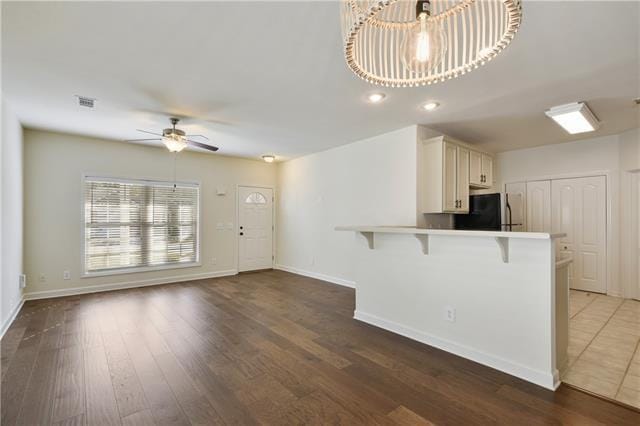 kitchen with ceiling fan, dark wood-type flooring, freestanding refrigerator, a peninsula, and a kitchen bar