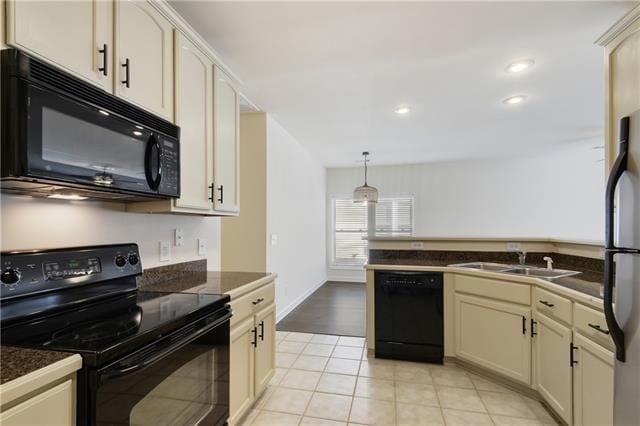 kitchen featuring dark countertops, cream cabinetry, black appliances, pendant lighting, and a sink