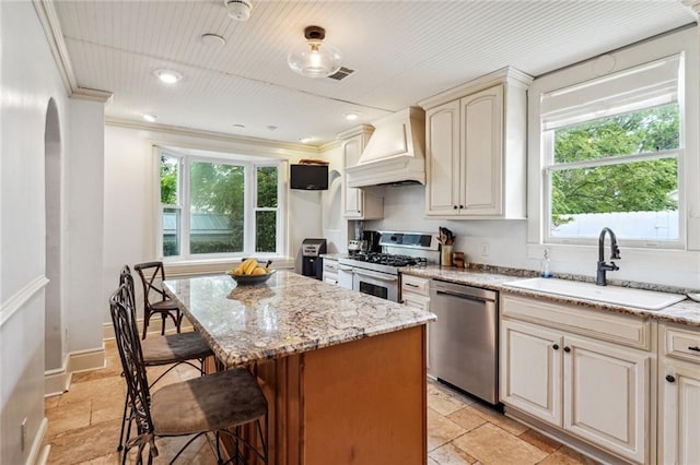 kitchen with stainless steel appliances, light stone countertops, sink, and custom range hood