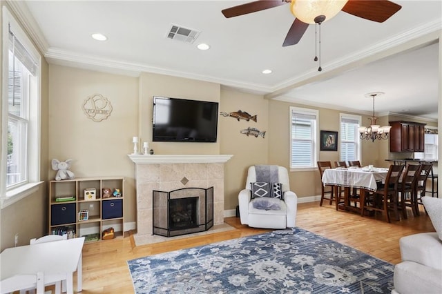 living room featuring a healthy amount of sunlight, ornamental molding, a tiled fireplace, and light hardwood / wood-style flooring