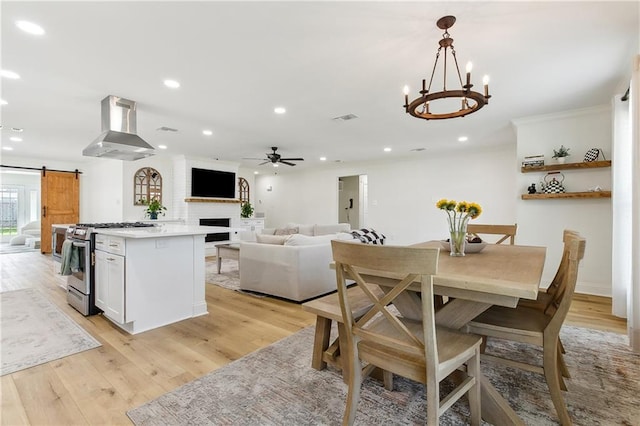 dining space featuring a barn door, ceiling fan with notable chandelier, and light hardwood / wood-style floors