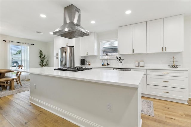 kitchen featuring a kitchen island, island range hood, white cabinets, stainless steel appliances, and light hardwood / wood-style flooring