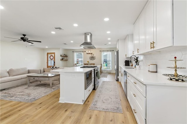 kitchen with a kitchen island, sink, white cabinets, light hardwood / wood-style floors, and wall chimney range hood