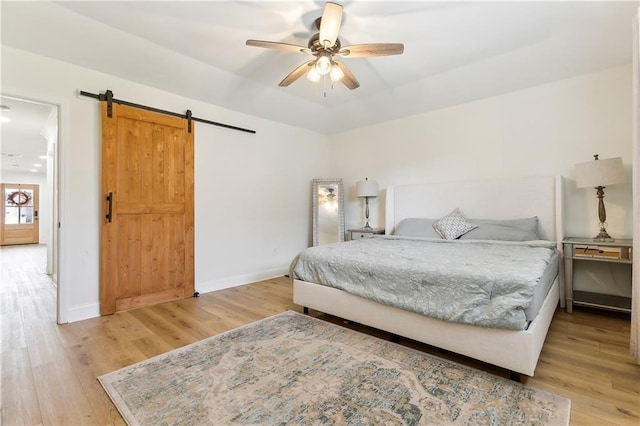 bedroom featuring a barn door, ceiling fan, and light hardwood / wood-style floors