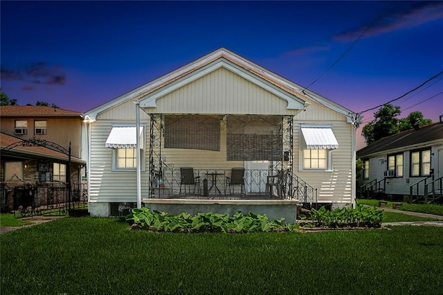 back house at dusk with covered porch and a lawn