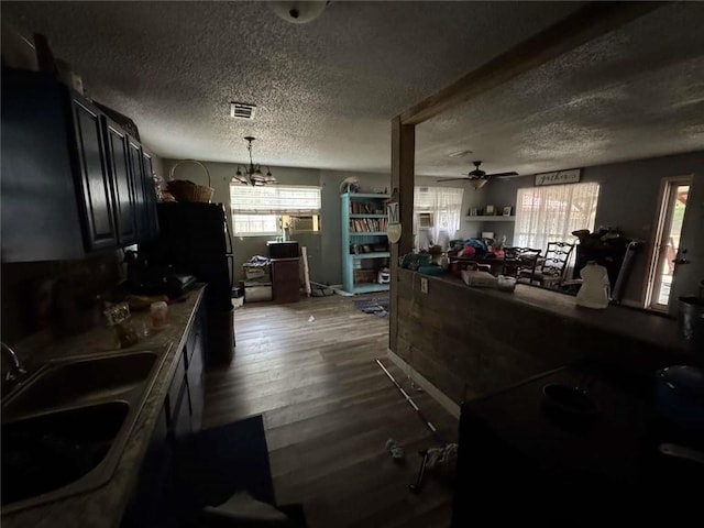 kitchen featuring sink, hanging light fixtures, black refrigerator, dark hardwood / wood-style floors, and ceiling fan with notable chandelier