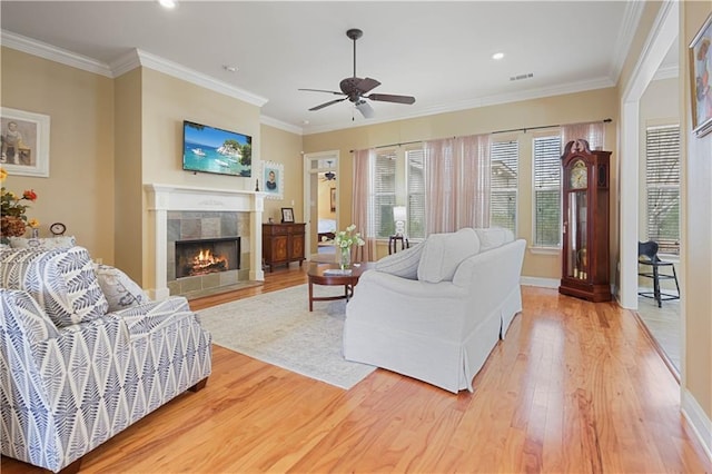 living room with a tiled fireplace, hardwood / wood-style floors, ornamental molding, and ceiling fan