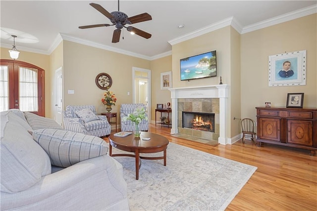 living room with a fireplace, ceiling fan, crown molding, light wood-type flooring, and french doors