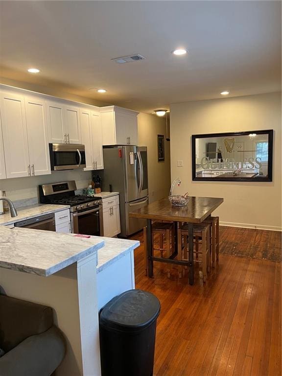 kitchen featuring appliances with stainless steel finishes, dark hardwood / wood-style floors, white cabinets, a kitchen breakfast bar, and kitchen peninsula