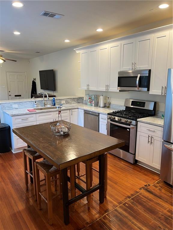 kitchen with appliances with stainless steel finishes, sink, white cabinets, ceiling fan, and kitchen peninsula