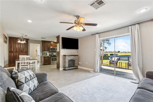 living room featuring ceiling fan, a stone fireplace, and light hardwood / wood-style flooring