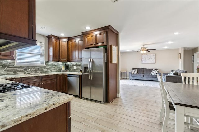 kitchen with light stone counters, tasteful backsplash, ceiling fan, stainless steel appliances, and light hardwood / wood-style floors