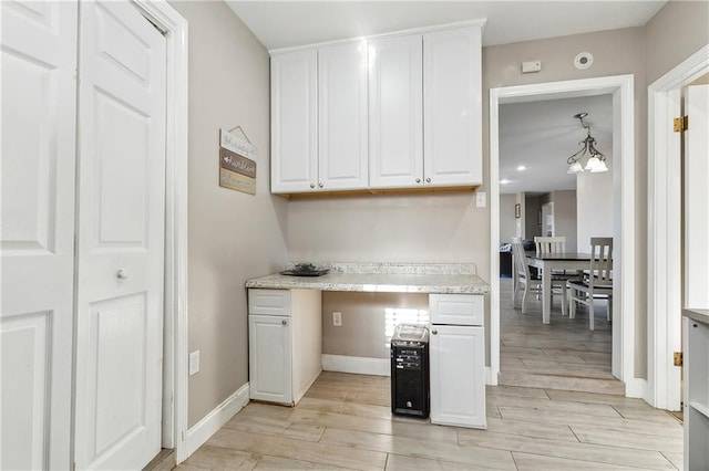 kitchen featuring white cabinetry, hanging light fixtures, built in desk, and light hardwood / wood-style floors