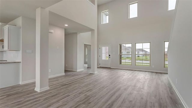 unfurnished living room featuring ornate columns, a towering ceiling, and light hardwood / wood-style floors