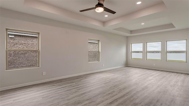 spare room featuring ceiling fan, a tray ceiling, and light wood-type flooring