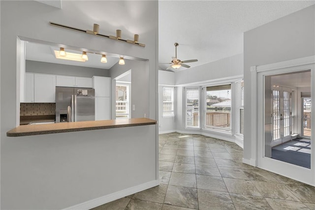 kitchen with white cabinetry, stainless steel fridge with ice dispenser, kitchen peninsula, ceiling fan, and decorative backsplash